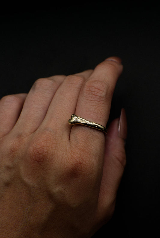 Hand wearing a gold bone ring on a dark background