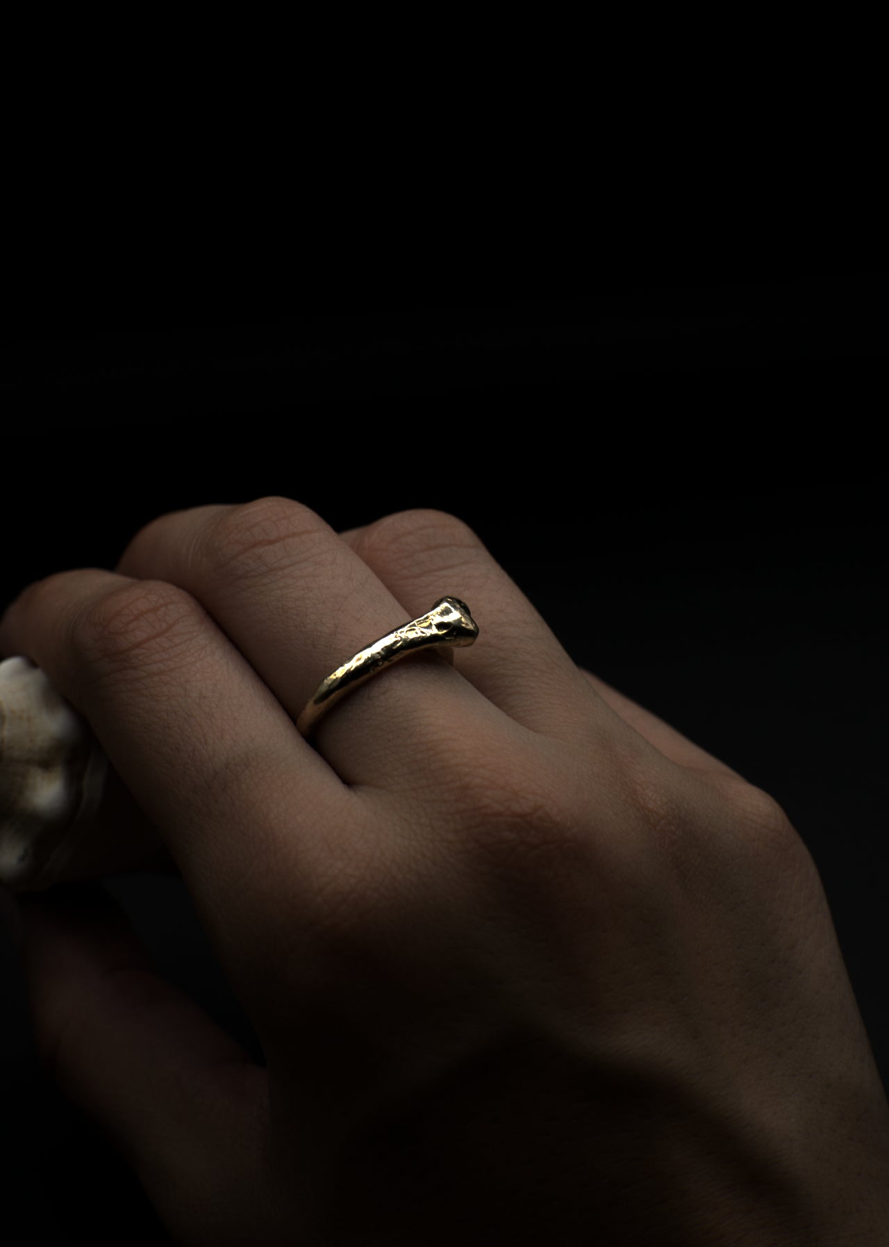 Gold bone ring on a finger against a dark background